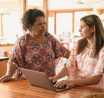 Two women in kitchen, young woman typing on computer listening to mature woman